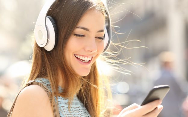 Portrait of a happy girl listening music on line with wireless headphones from a smartphone in the street in a summer sunny day; Shutterstock ID 379883392; user id: 13188350; user email: foy.song@pearson.com; user_country: China; discount: 20%